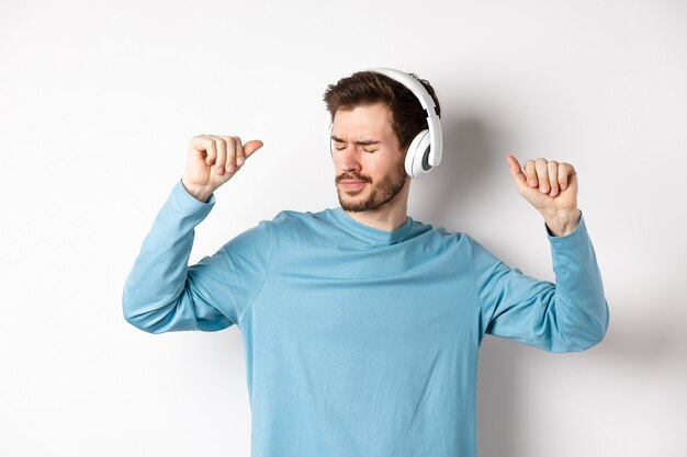 Felice giovane uomo divertirsi in cuffia, ballare mentre si ascolta la musica in auricolari wireless, sfondo bianco.