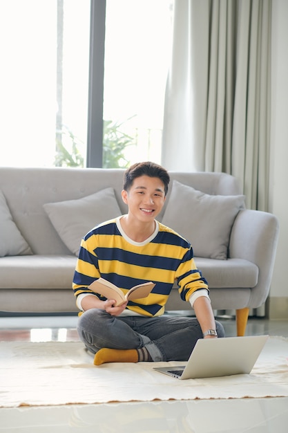 Felice giovane uomo seduto su un pavimento con un computer portatile in un soggiorno.