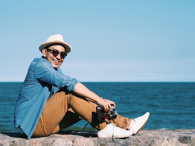 Felice giovane viaggiatore uomo seduto sulla spiaggia.