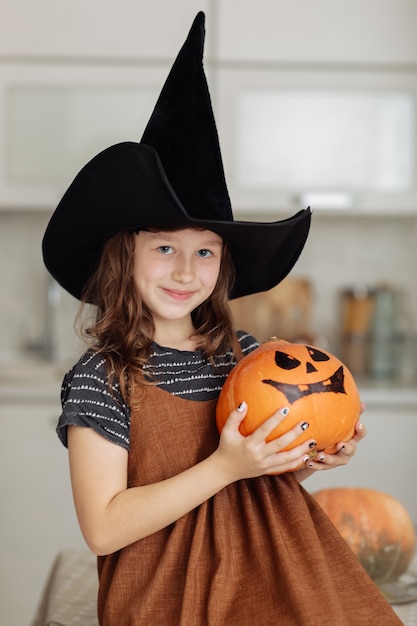 Felice Halloween. Bambina sveglia in costume da strega con zucca intagliata. Famiglia felice che si prepara per Halloween.