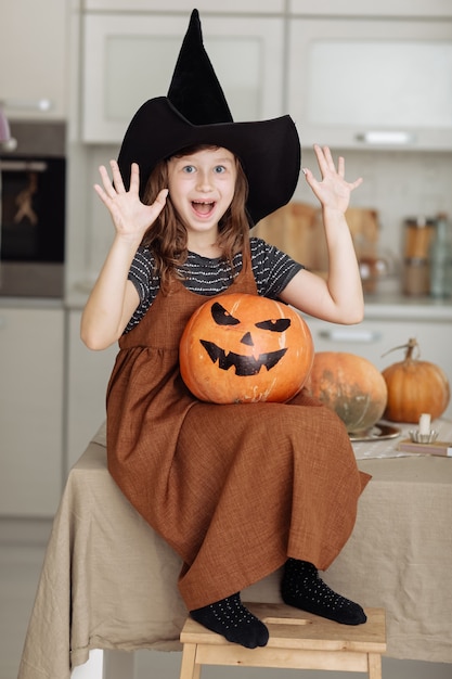 Felice Halloween. Bambina sveglia in costume da strega con zucca intagliata. Famiglia felice che si prepara per Halloween.