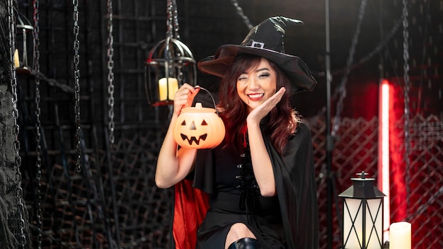 Felice halloween giovane donna asiatica in costume nero che indossa un cappello da strega che porta zucca lanterna Sorriso di emozione