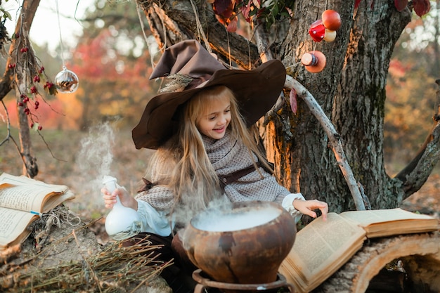 Felice Halloween. Una ragazza carina in costume da strega è nella tana della strega. La piccola strega allegra e carina prepara una pozione magica. Halloween.