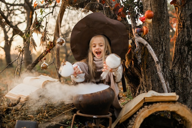 Felice Halloween. Una ragazza carina in costume da strega è nella tana della strega. La piccola strega allegra e carina prepara una pozione magica. Halloween.