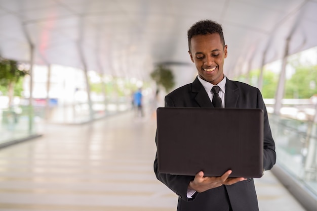 Felice imprenditore africano all'aperto utilizzando il computer portatile mentre sorridendo