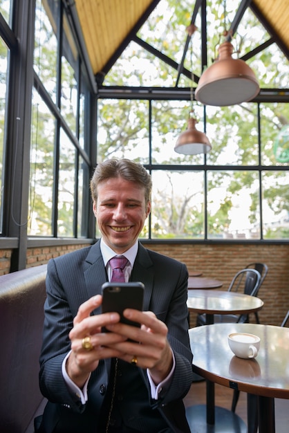 Felice imprenditore sorridente e utilizzando il telefono cellulare nella caffetteria