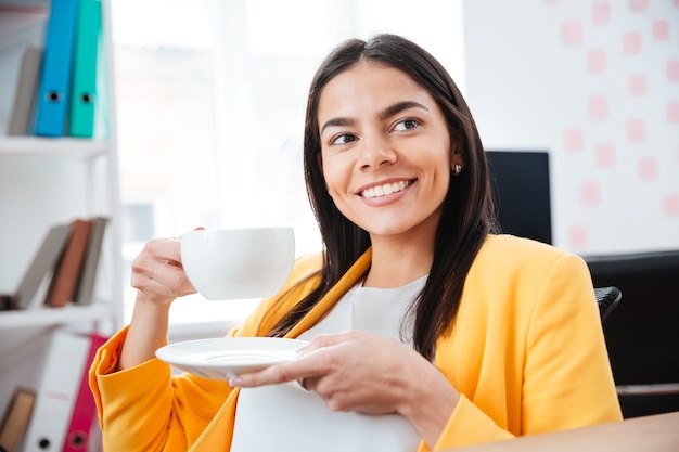 Felice imprenditrice che beve il tè in ufficio