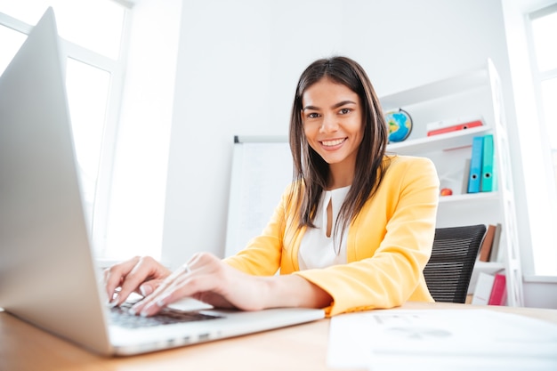 Felice imprenditrice che utilizza il computer portatile e guarda davanti in ufficio