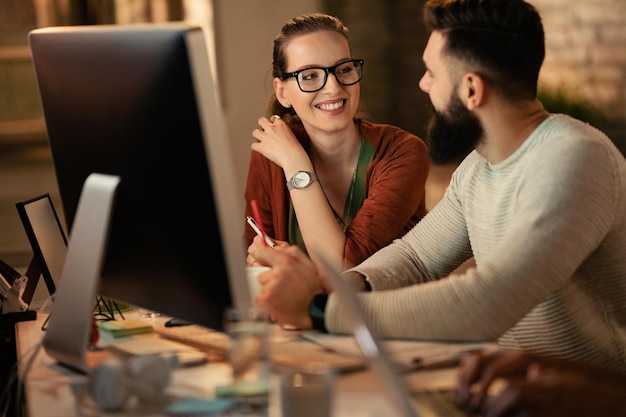 Felice imprenditrice creativa che parla con il suo collega mentre lavora in ufficio