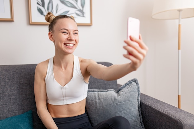 Felice influencer femminile in abbigliamento sportivo che ride e parla con il pubblico durante la trasmissione in diretta da casa