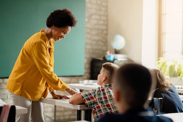 Felice insegnante afroamericano che parla con uno scolaro durante una lezione in classe