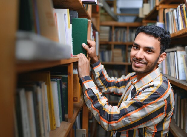 Felice intelligente ragazzo indiano o arabo studente universitario maschio di razza mista nella biblioteca