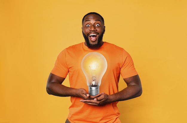 Felice l'uomo afro tiene una lampadina con le mani.