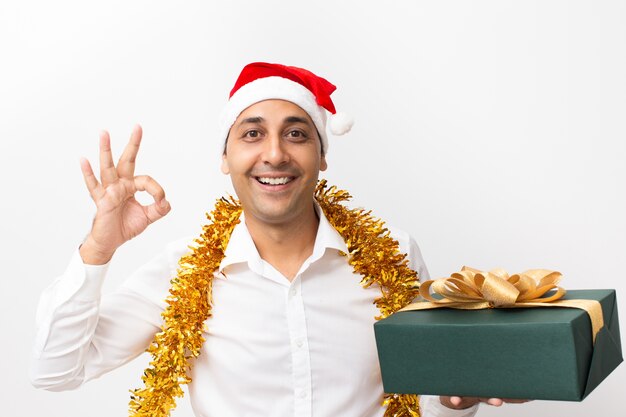 Felice l&#39;uomo mostrando il segno giusto con il tinsel e la confezione regalo