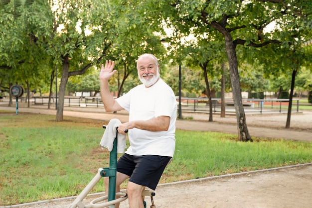 Felice l'uomo più anziano che si esercita presso la palestra all'aperto nel parco guarda la telecamera e ondeggia