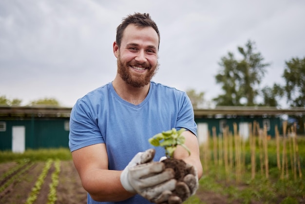 Felice lavoratore agricolo con una pianta in un'azienda agricola con un sorriso Agricoltore che fa pubblicità alla crescita della sostenibilità e all'ecologia su un campo verde o un terreno in una campagna ambientale ecologica della natura