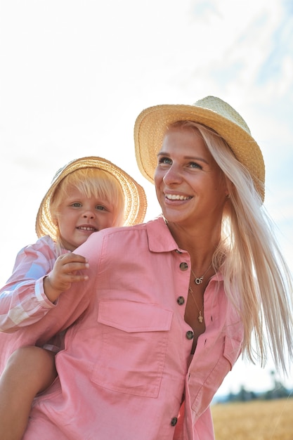 Felice madre che tiene bambino sorridente su un campo di grano alla luce del sole.