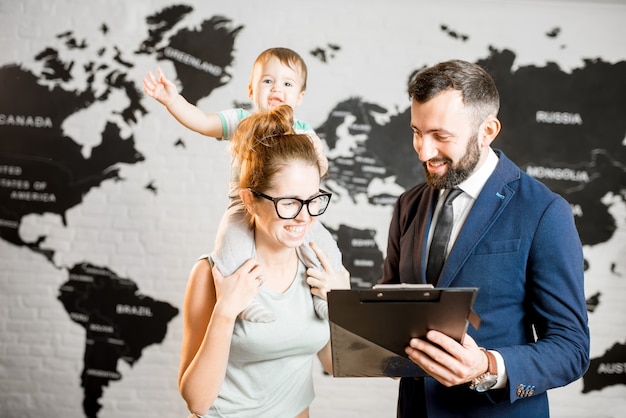 Felice madre e bambino che scelgono il tour per una vacanza estiva con un agente maschile presso l'ufficio dell'agenzia di viaggi con la mappa del mondo sullo sfondo