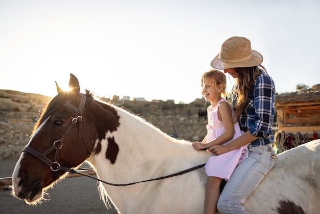 Felice madre e figlia a cavallo al tramonto