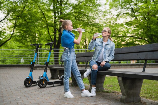 Felice madre e figlia con scooter elettrici stanno bevendo limonata nel parco cittadino