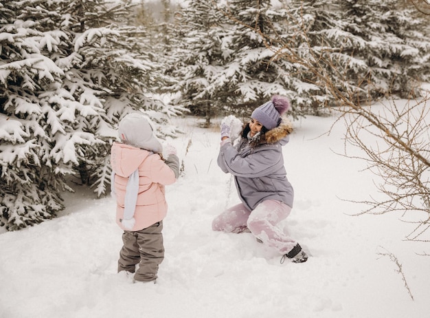 Felice madre e figlia giocano a palle di neve in un parco naturale innevato in una nevicata. Grande momento divertente. Trascorrere del tempo insieme in una bella fredda giornata invernale.
