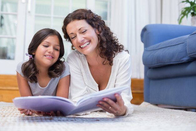 Felice madre e figlia sdraiata sul pavimento e leggendo un libro