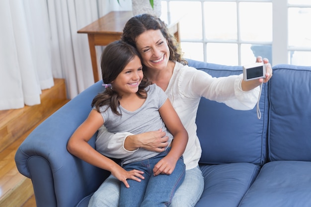 Felice madre e figlia seduta sul divano e prendendo selfie