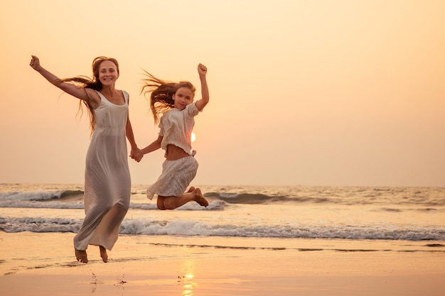 Felice madre e figlia sulla spiaggia al tramonto divertendosi in riva al mare. giocando a saltare e gioire donna e suo figlio copia spazio copyspace