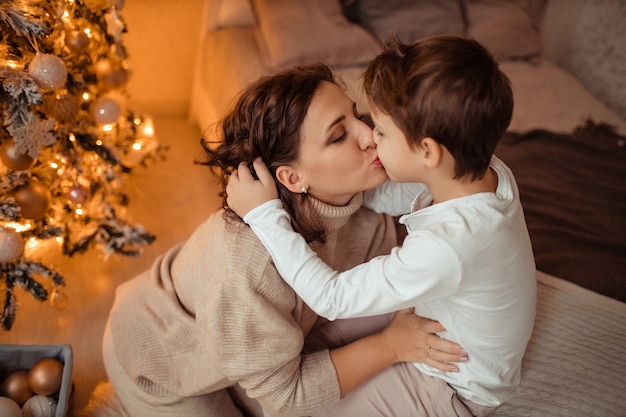 Felice madre e figlio a casa in camera da letto vicino all'albero di Natale
