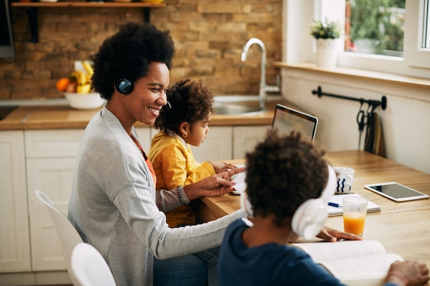 Felice madre nera che lavora mentre i suoi figli stanno imparando a casa