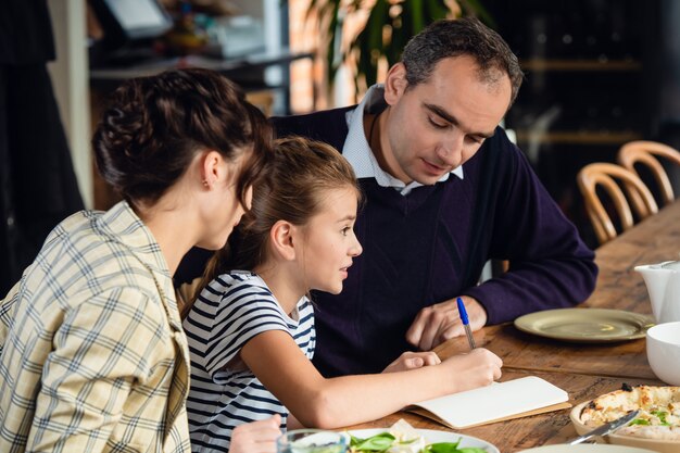 felice madre, padre e bambina cenando e parlando al ristorante o al caffè