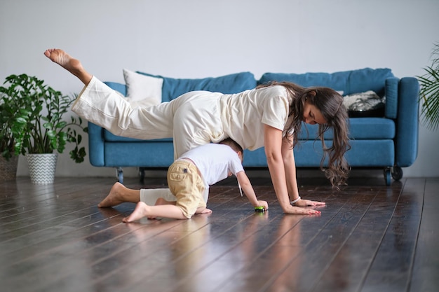 Felice madre single consapevole che fa esercizi mattutini in posa yoga con bambino che gioca a casa esercizi mattutini in pigiama bambino interferisce con l'allenamento