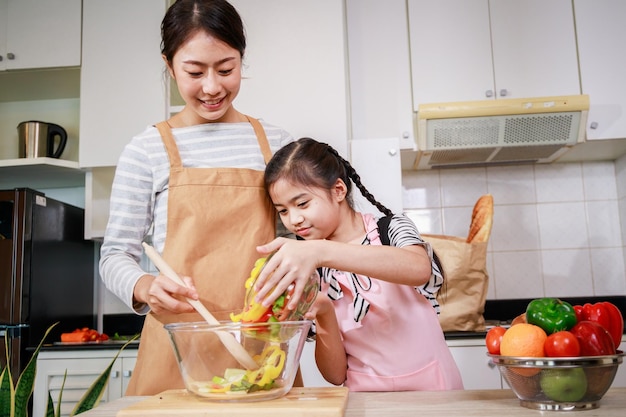 Felice mamma e figlia che aiutano a preparare insalata di verdure in cucina a casa