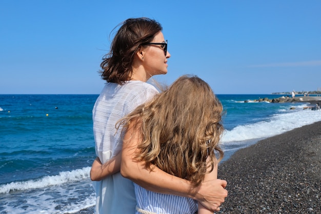 Felice mamma e figlia che si abbracciano camminando insieme lungo la spiaggia, vista posteriore. Famiglia, vacanza, felicità, infanzia, comunicazione madre e figlio