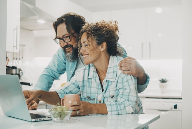 Felice marito e moglie che si godono il tempo in cucina utilizzando il computer portatile giovane coppia guardando lo schermo del notebook navigando in internet scegliendo di fare shopping online insieme in appartamento Persone tecnologia