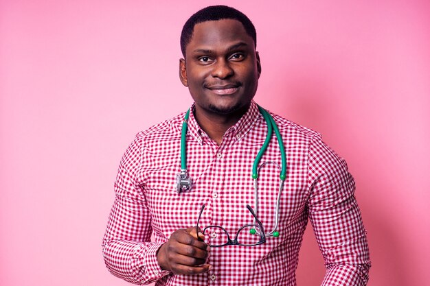 Felice maschio africano chirurgo medico cardiologo medico in camice bianco su sfondo rosa in studio.