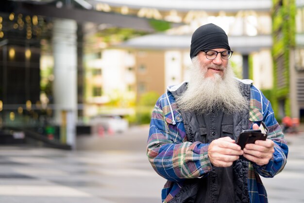 Felice maturo barbuto hipster uomo utilizzando il telefono nelle strade della città all'aperto