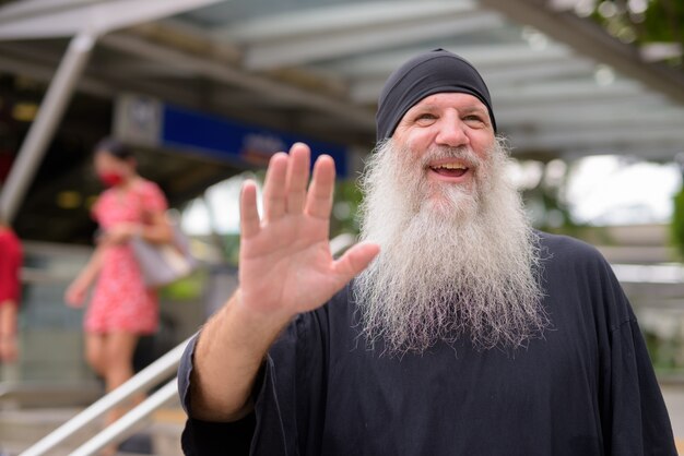 Felice maturo bello barbuto hipster uomo agitando la mano fuori dalla stazione della metropolitana