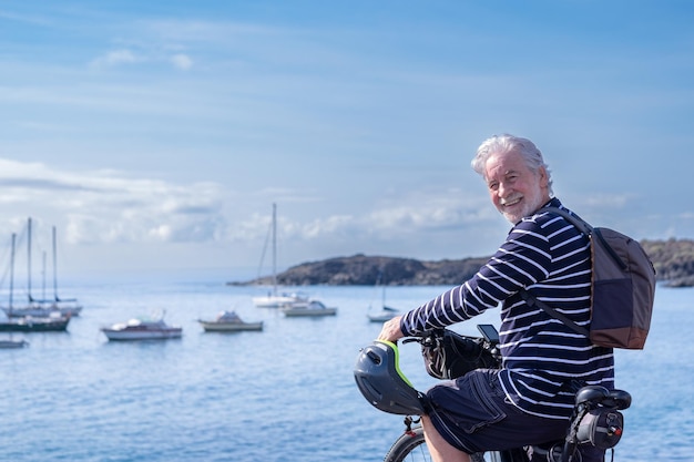 Felice maturo ciclista senior uomo sorridente in piedi davanti al mare guardando la fotocamera Uomo anziano con bicicletta godendo la vacanza in pensione libertà e stile di vita sano Orizzonte sull'acqua