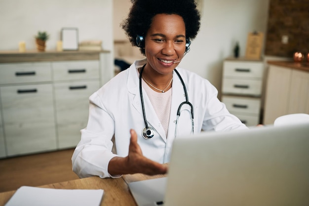 Felice medico afroamericano che parla durante la videochiamata sul laptop nel suo ufficio