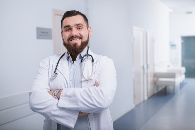 Felice medico con la barba che sorride alla macchina fotografica, godendo di lavorare in un ospedale moderno