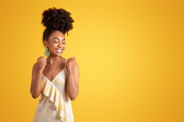 Felice millenaria donna afroamericana in abito che fa un gesto di successo che celebra la vittoria