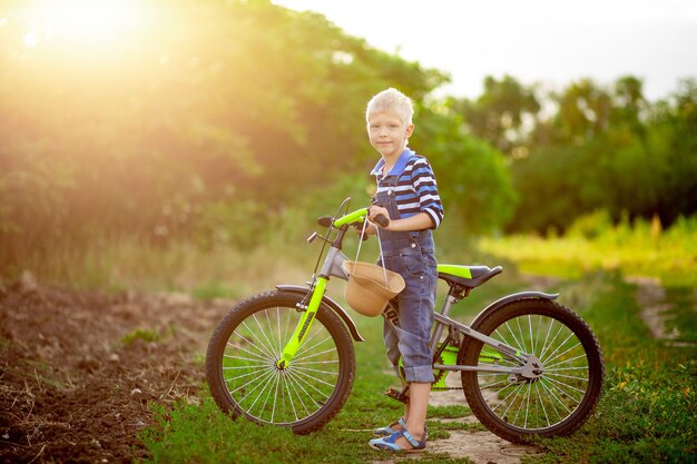 Felice neonato biondo con una bicicletta si trova in un campo in estate, lo stile di vita dei bambini