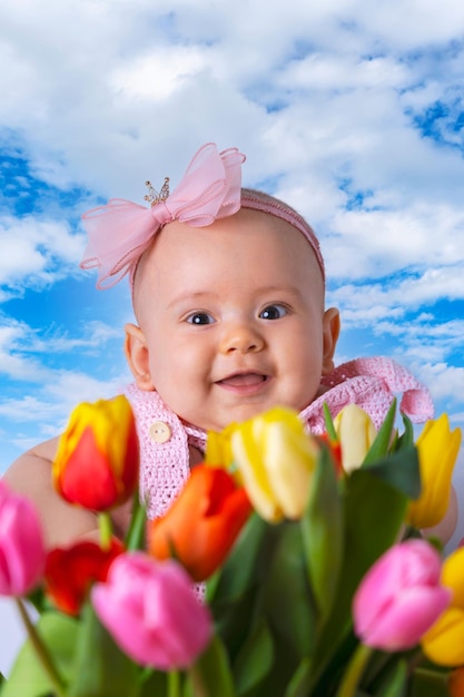 Felice neonato su uno sfondo di cielo blu e accanto a tulipani multicolori