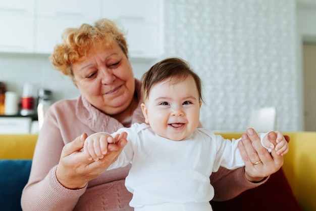 Felice nonna caucasica che gioca e tiene in braccio la sua nipotina a casa. Affettuosi nonni e nipoti di due generazioni di due generazioni si godono il tempo insieme