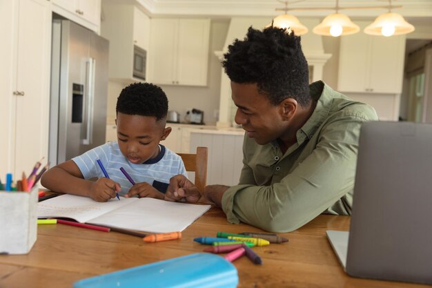 Felice padre afroamericano con il figlio che fa i compiti a casa sorridendo. vita domestica familiare, trascorrere del tempo lavorando insieme a casa.