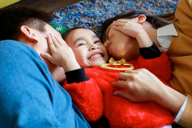 Felice padre di famiglia asiatica, madre e figlia indossano un maglione con il rosso sdraiato sul pavimento del tappeto per celebrare insieme la vigilia di Natale.