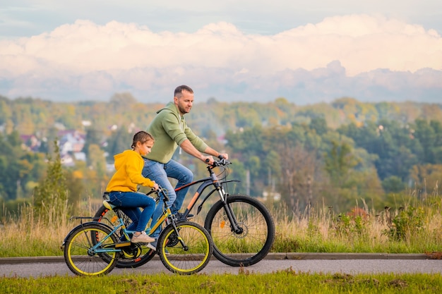 Felice padre e figlia fanno un giro in bicicletta nella natura in autunno.