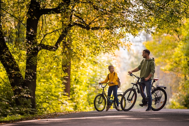 Felice padre e figlia fanno un giro in bicicletta nella natura in autunno.