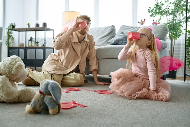 Felice padre e figlia piccola che indossano come fate magiche che giocano a tea party nel soggiorno di casa